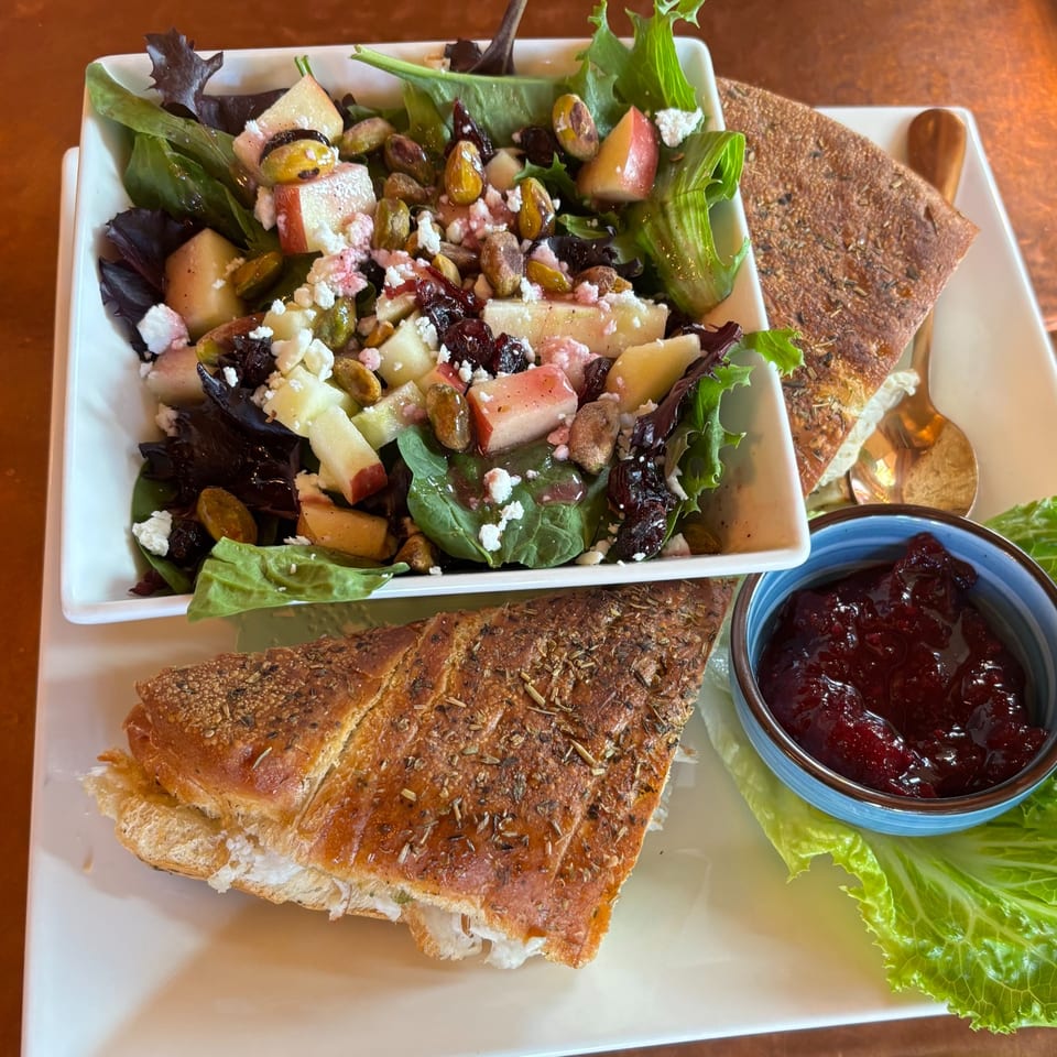 A fresh salad with apples, pistachios, and feta, alongside a sandwich and cranberry sauce.
