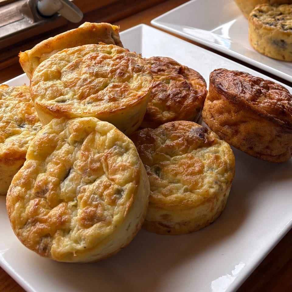 Several golden-brown mini quiches or frittatas on white rectangular plates, ready to be served.
