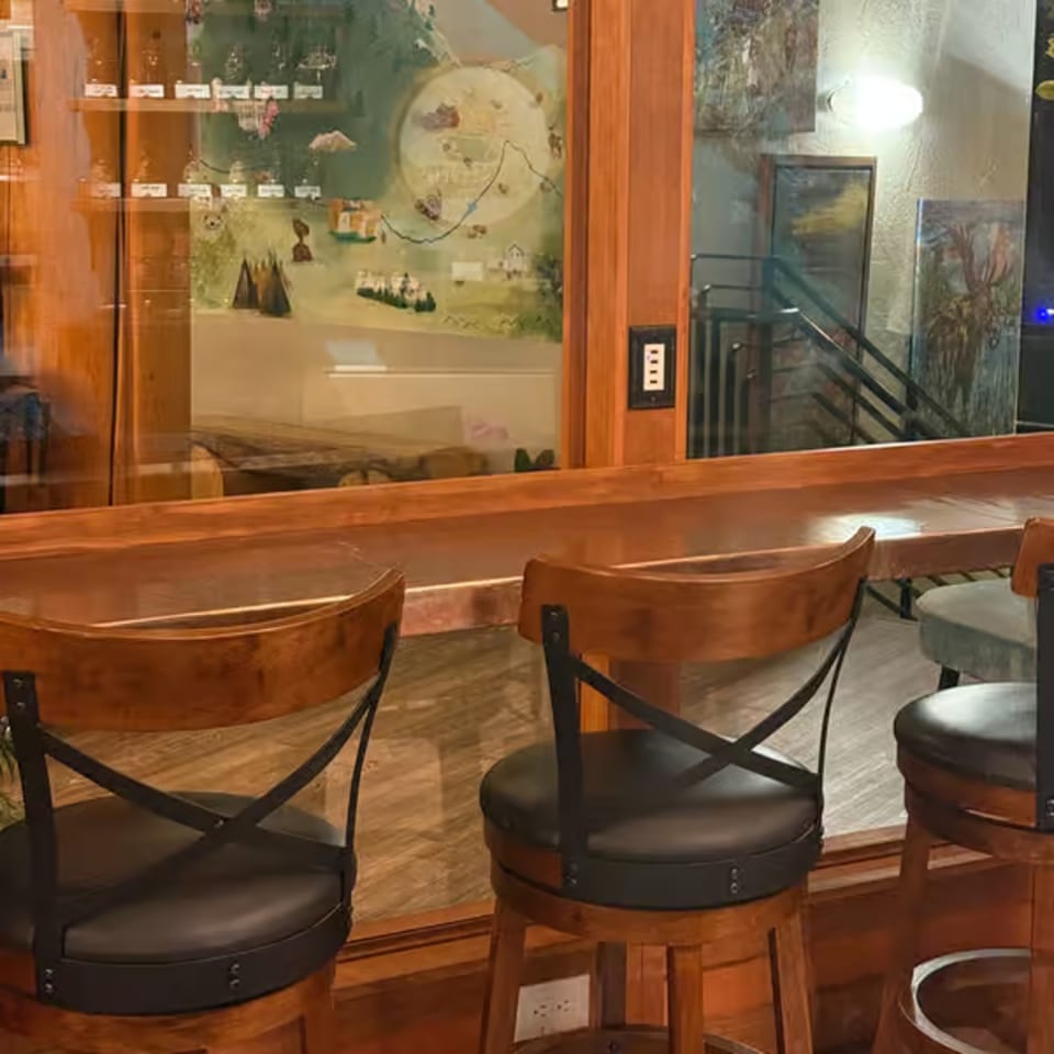 Wooden bar with three bar stools, a mural, and paintings on the wall.