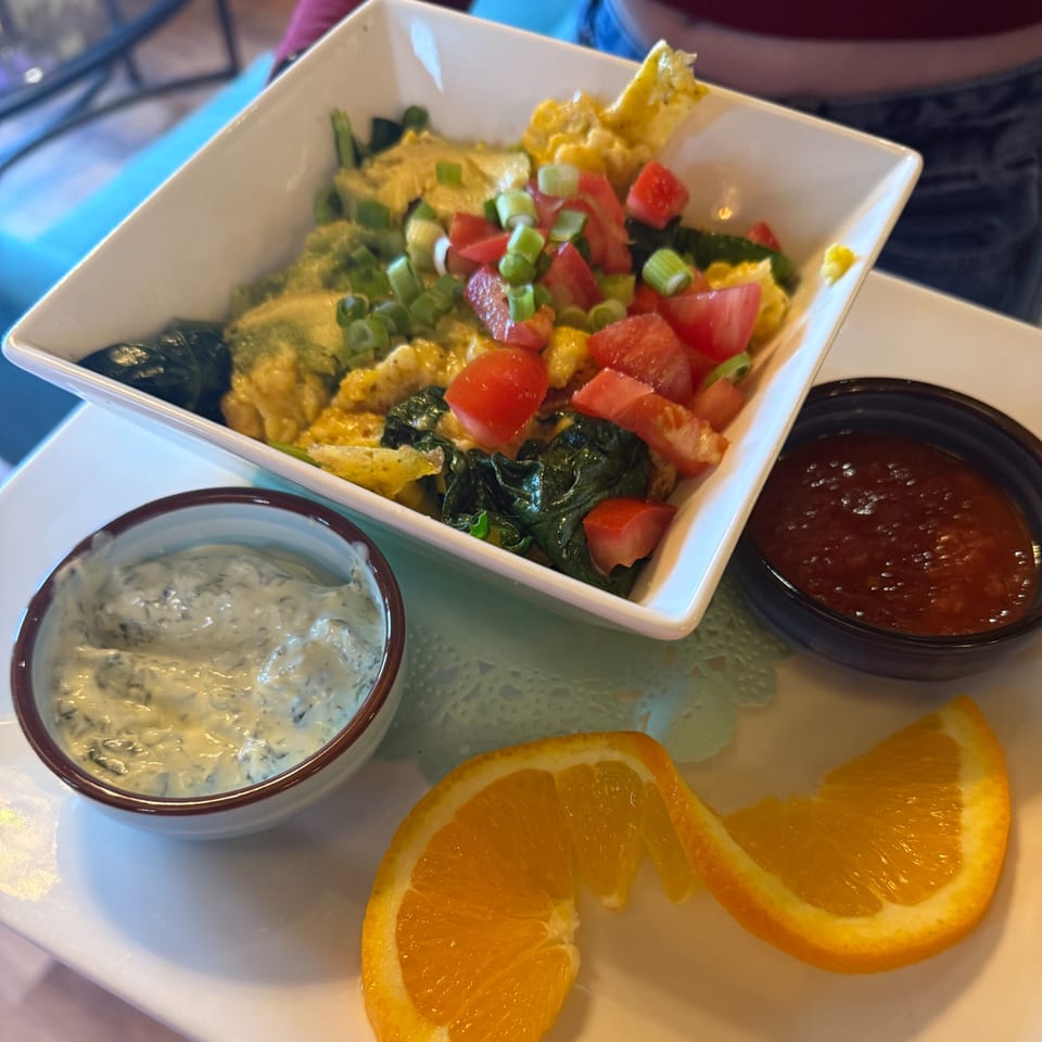 Scrambled eggs with spinach, tomatoes, and green onions, served with two sauces and orange slices.