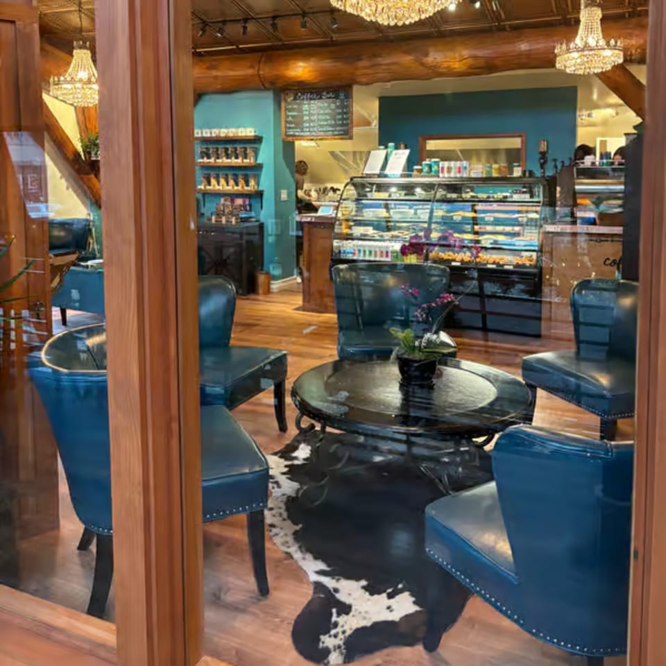 A cozy cafe interior with blue leather chairs, a round table, and a display case of pastries.