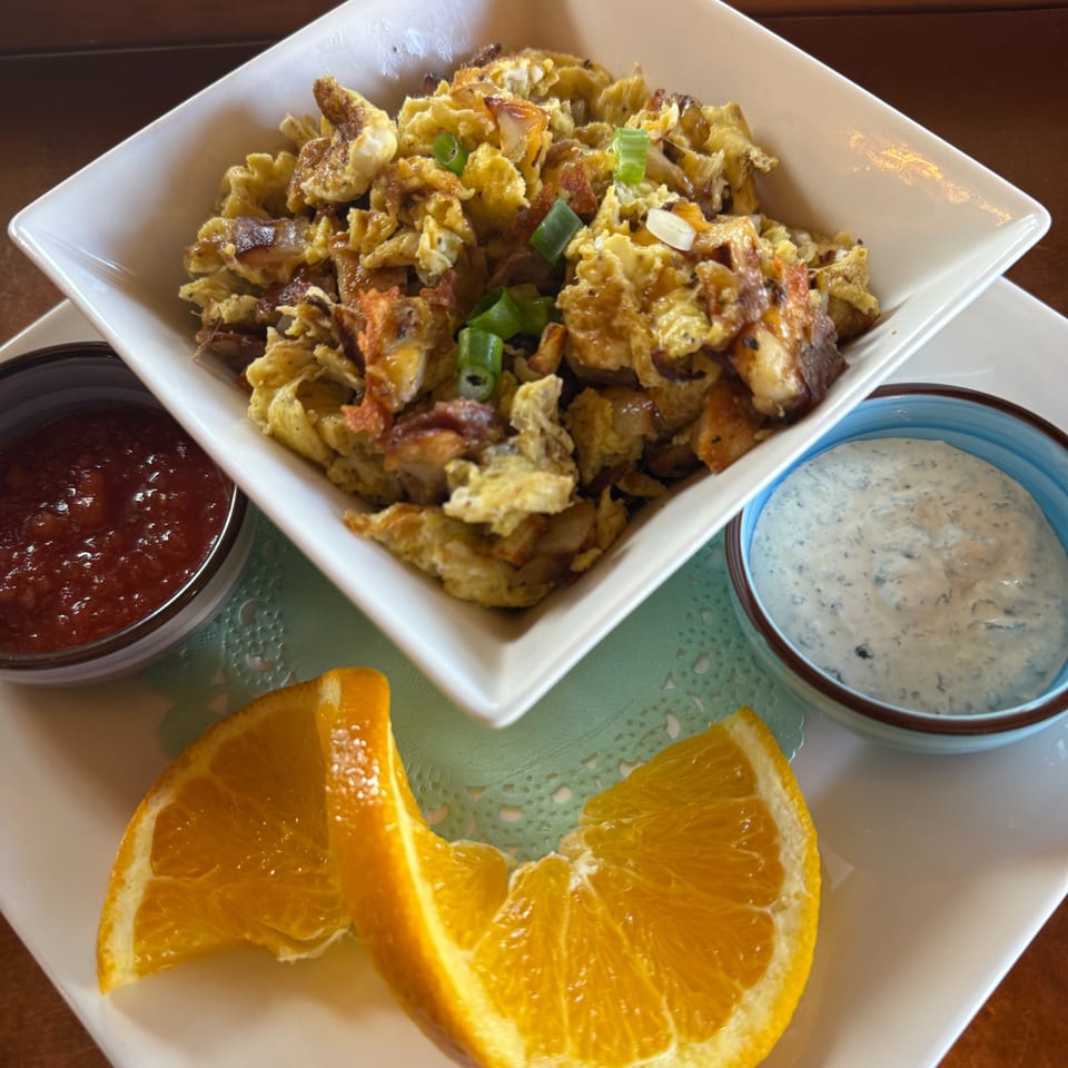 Scrambled eggs with green onions, salsa, ranch, and orange slices on a white plate.