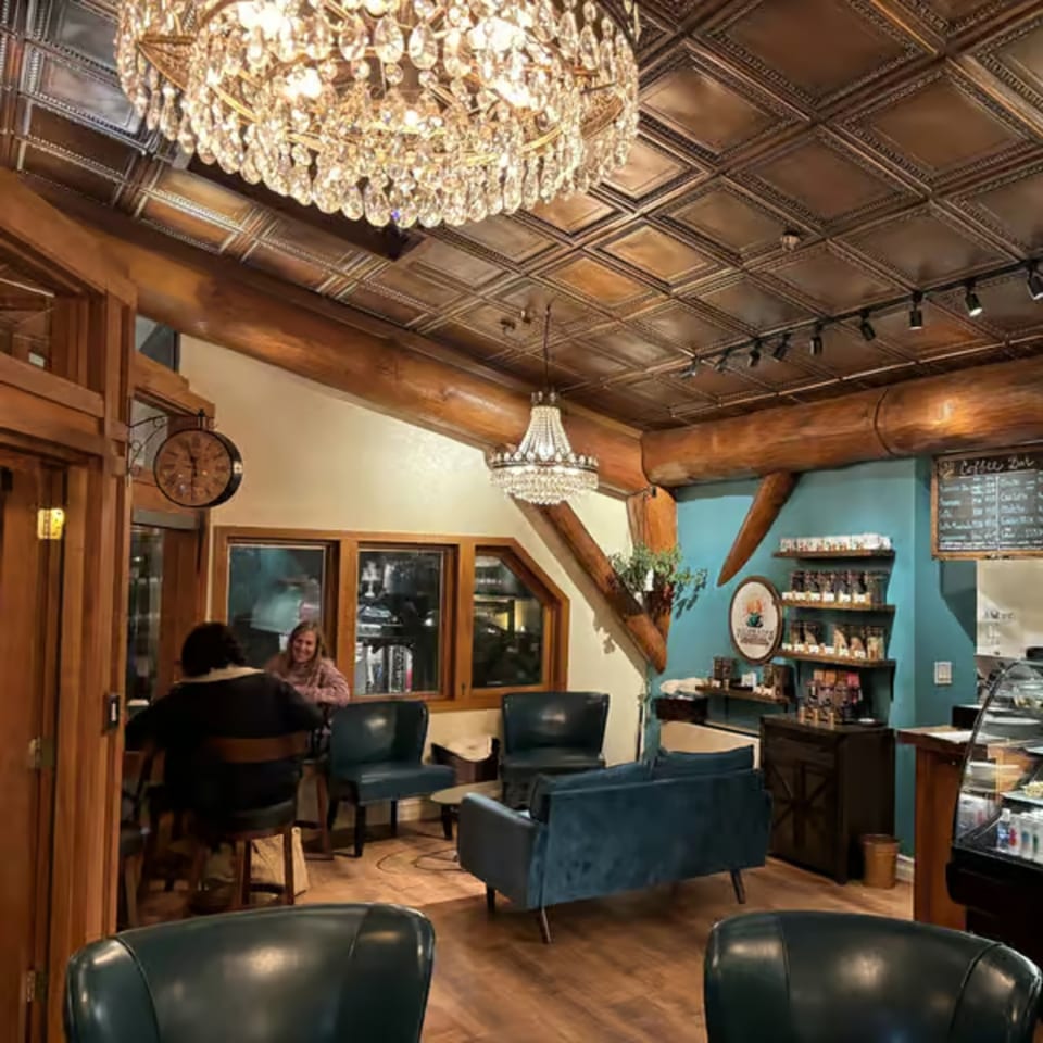 Cozy coffee shop interior with chandeliers, teal walls, wooden beams, and customers seated.