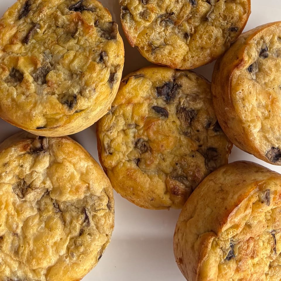 Six golden-brown muffins with dark chocolate chips scattered on a white surface.